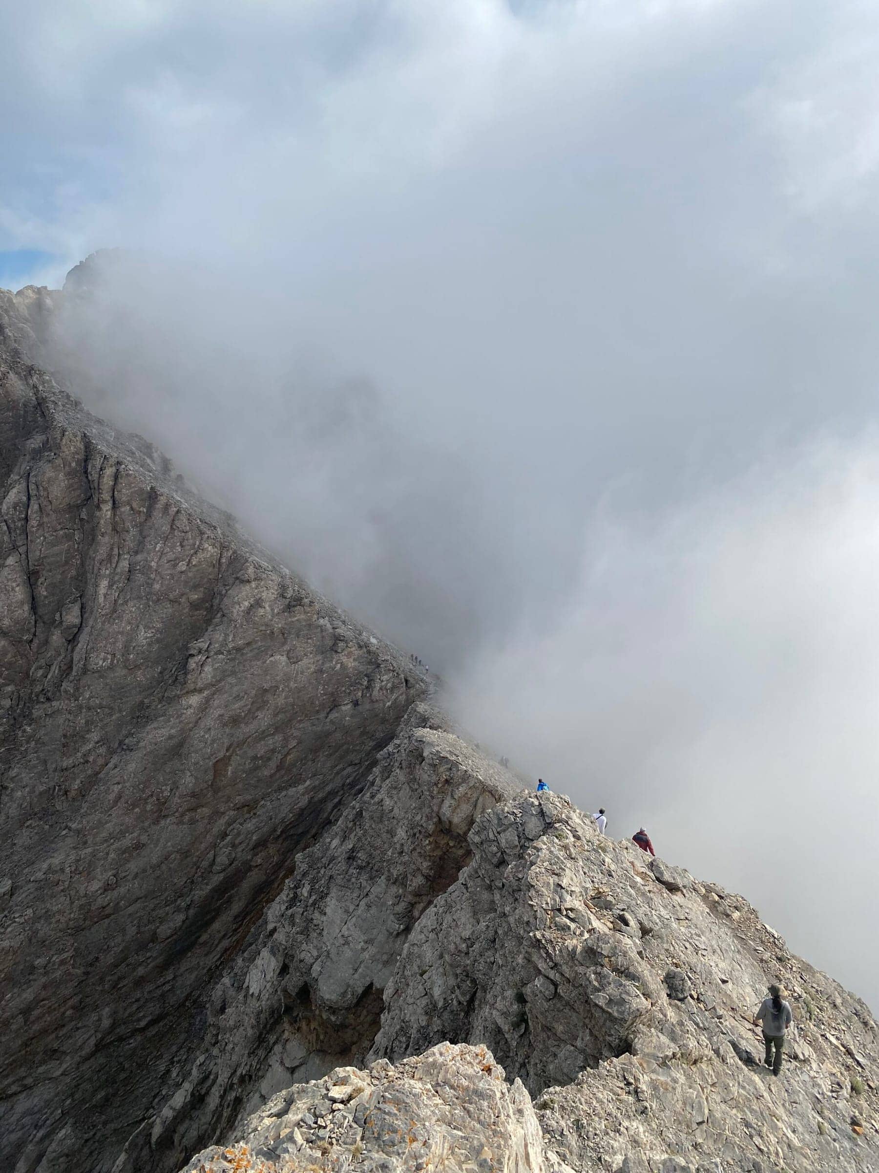 Climbers carefully navigating the rock bridge between Skala and Mytikas