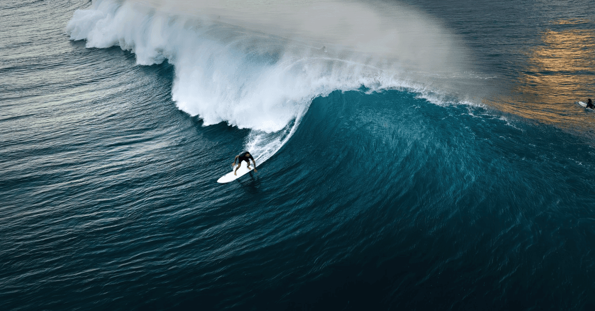 Aerial view of a surfer dropping down the face of a large, glassy wave